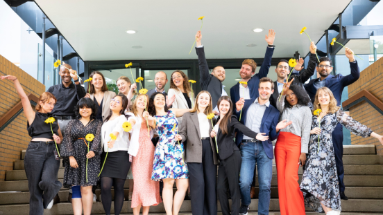 Graduates from the Master's programme on a set of stairs, each holding a yellow flower